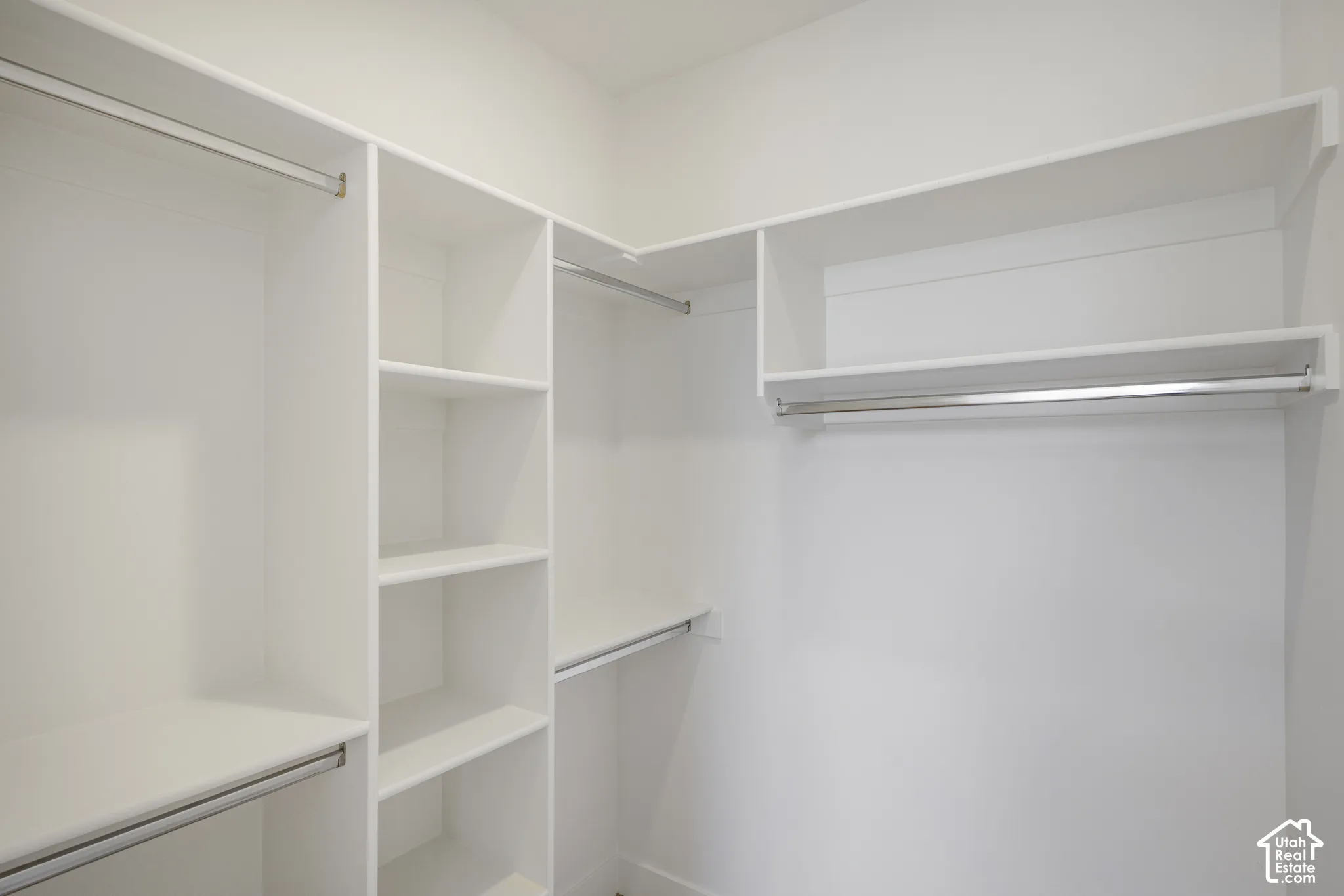 Walk-in closet featuring white built-in shelving, multiple open storage compartments, and metal clothing rods