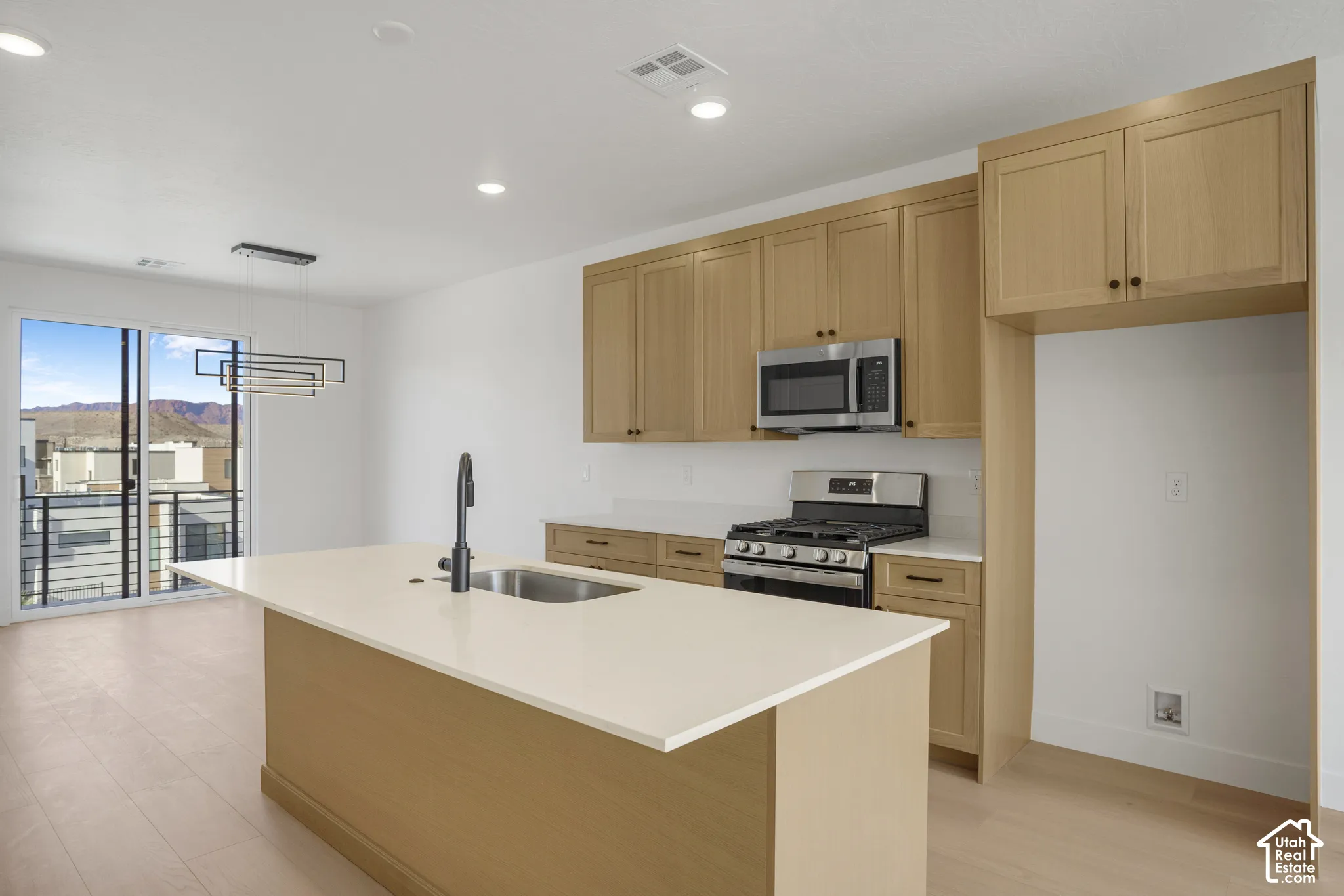 Kitchen featuring flat-panel wood cabinetry, quartz countertops, central island with undermount sink, stainless steel gas range, and wood-finish flooring