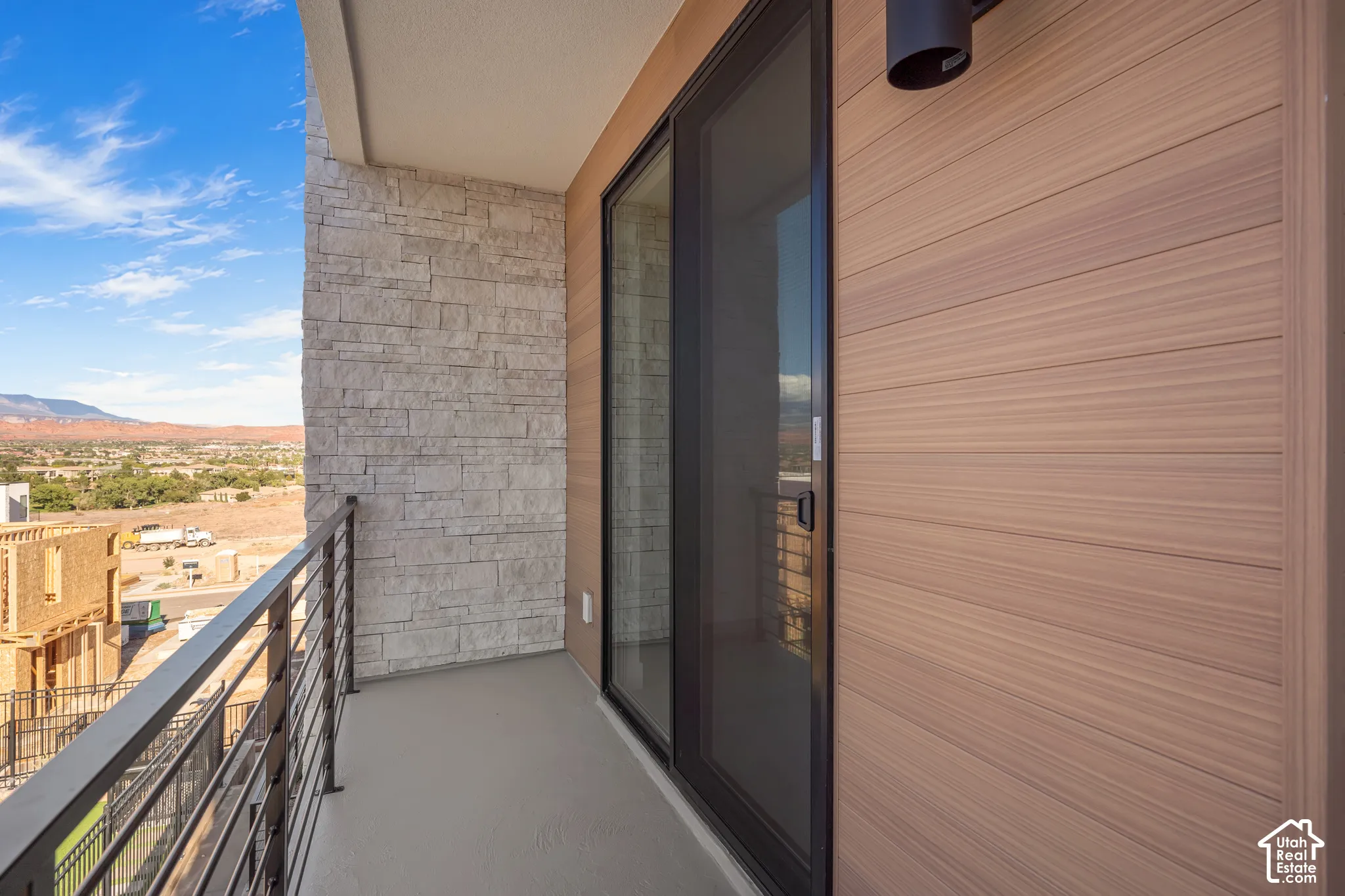 Private balcony featuring stacked stone masonry, wood-finish siding, a metal cable railing, and sliding glass door entry