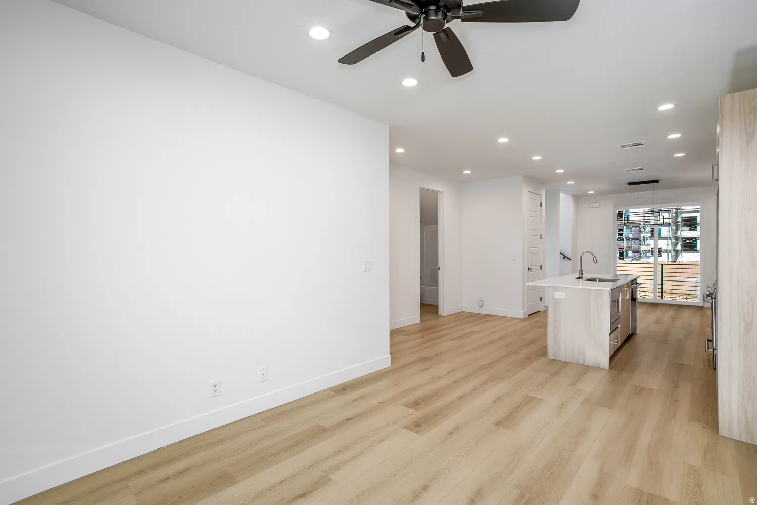 Kitchen featuring a center island with sink, recessed lighting, a ceiling fan, light wood-style flooring, and light stone counters