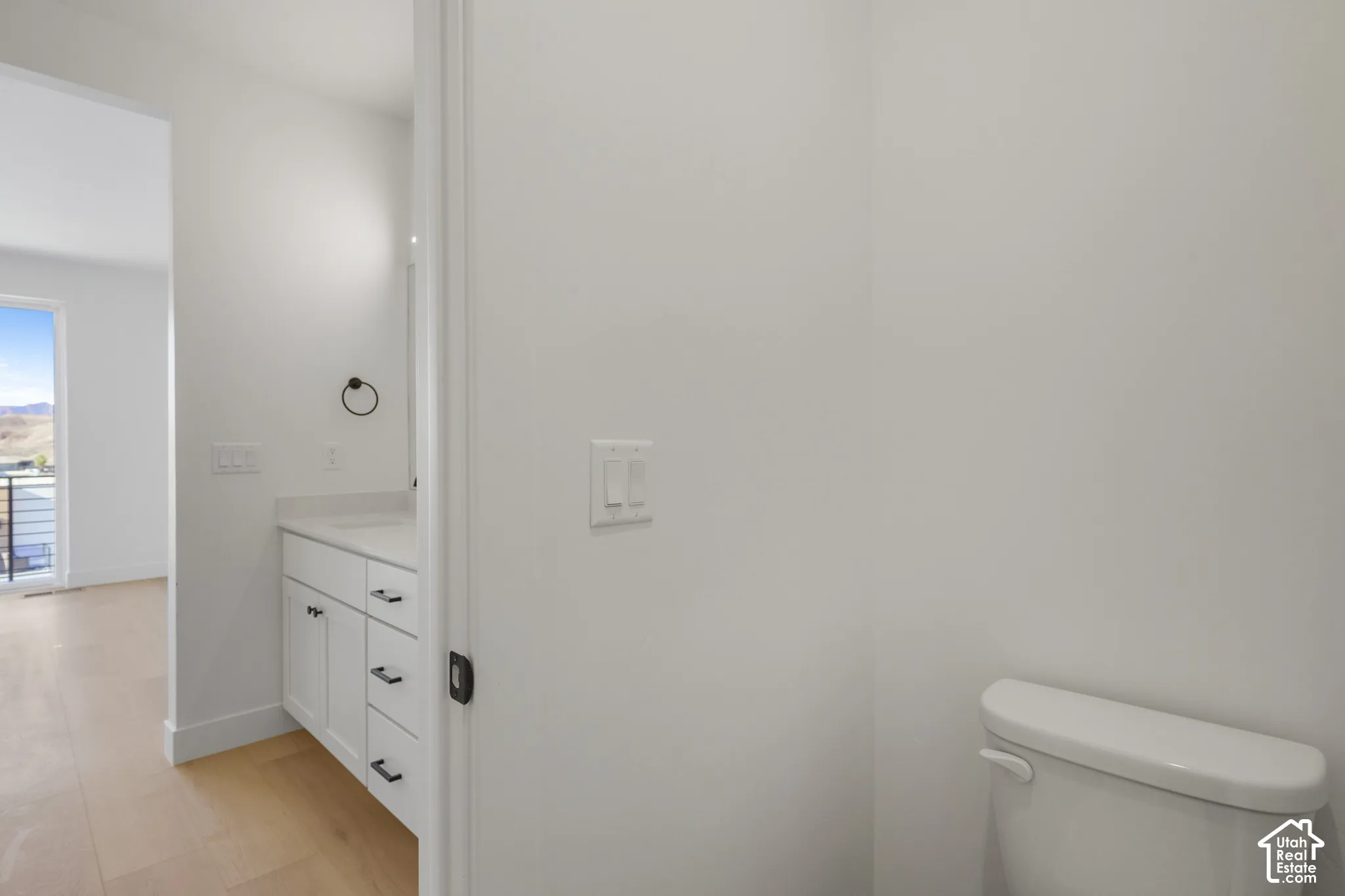 White vanity cabinetry with shaker-style doors, light-toned stone-finish countertop, undermount sink, and matte black hardware featuring wood-finish flooring