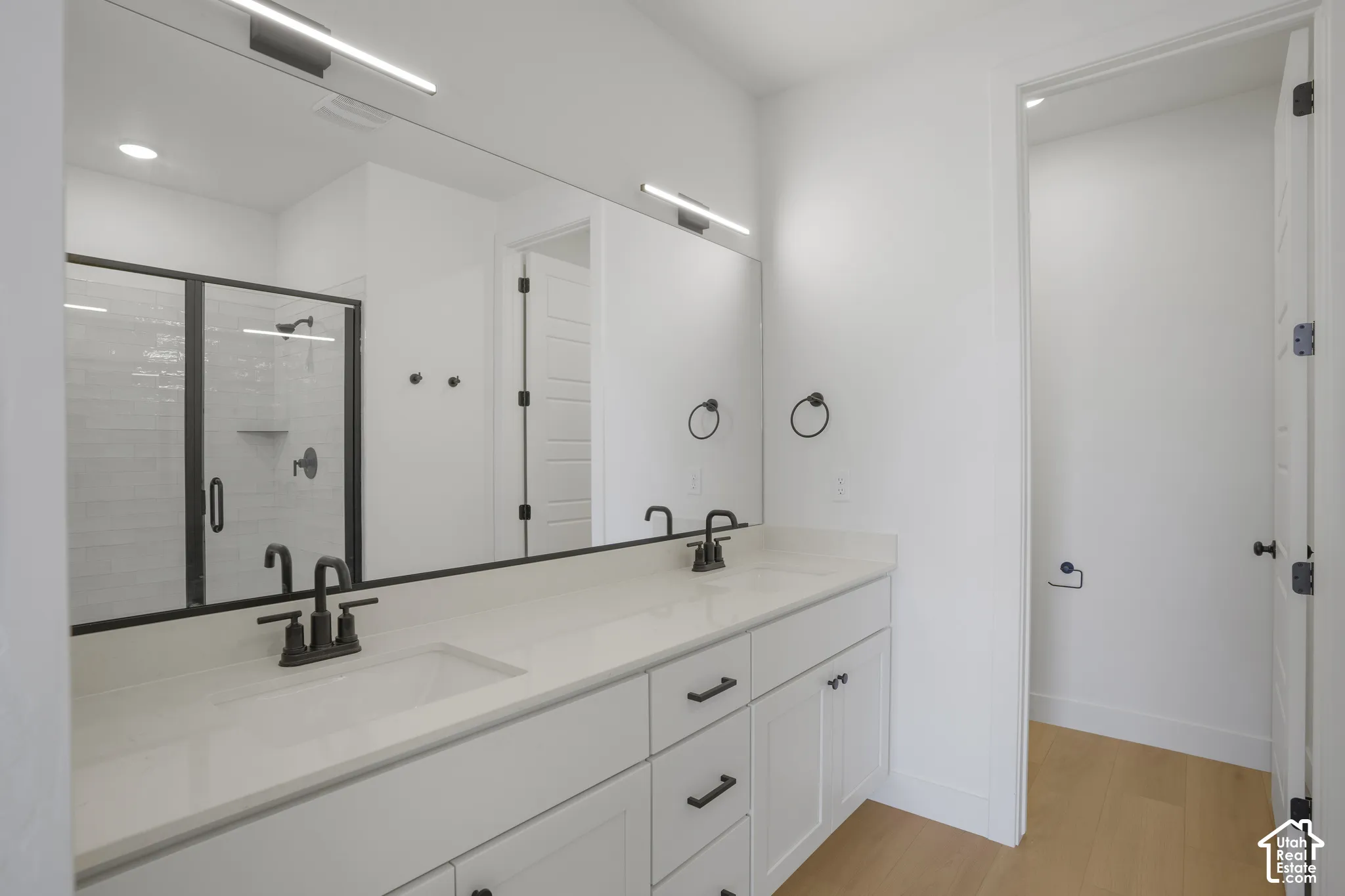 Double vanity featuring white cabinetry, quartz countertop, matte black hardware, and an expansive wall-to-wall mirror with integrated linear lighting