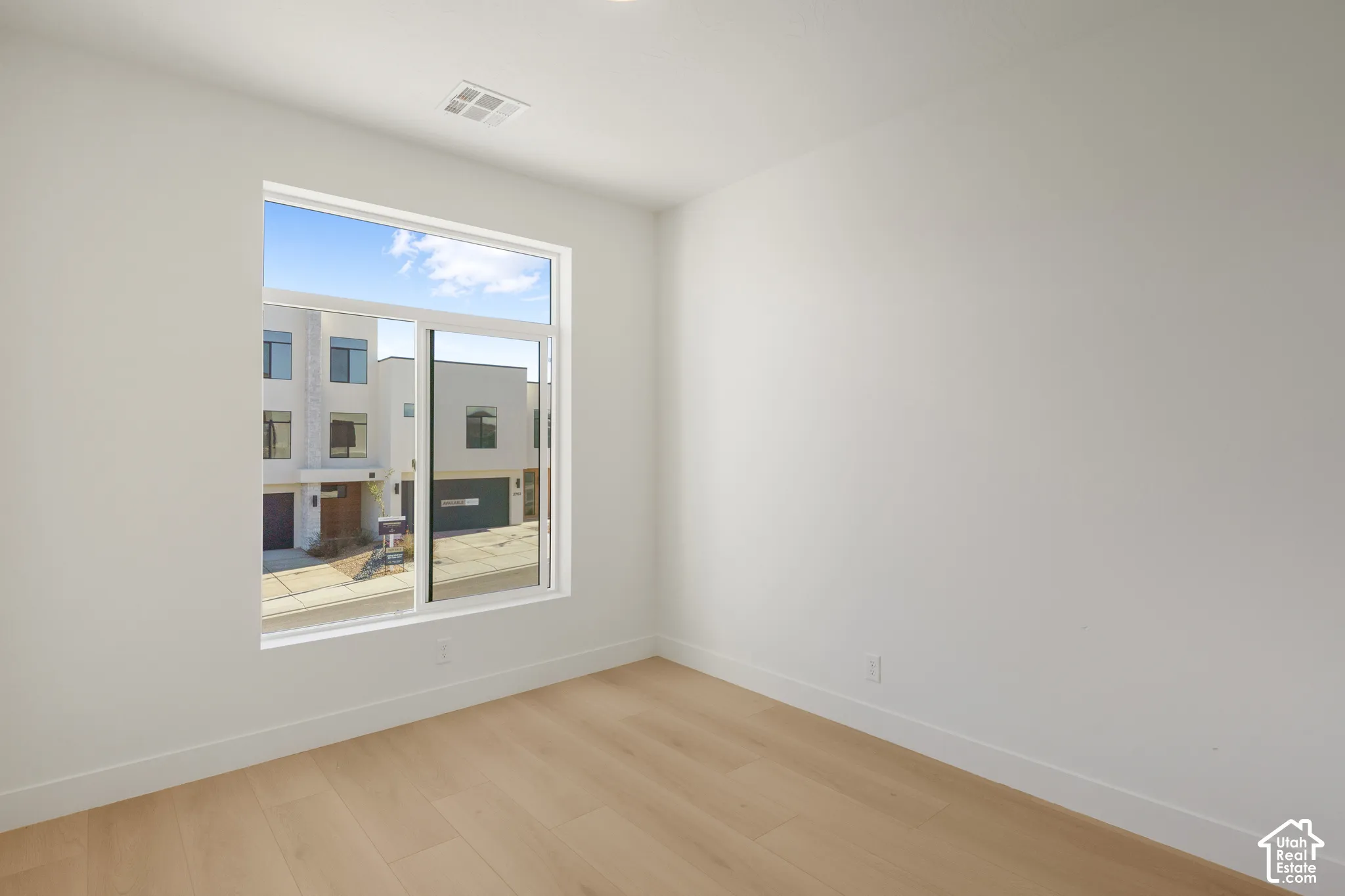 Neutral interior featuring light-tone wood-finish flooring, expansive floor-to-ceiling windows, and white walls