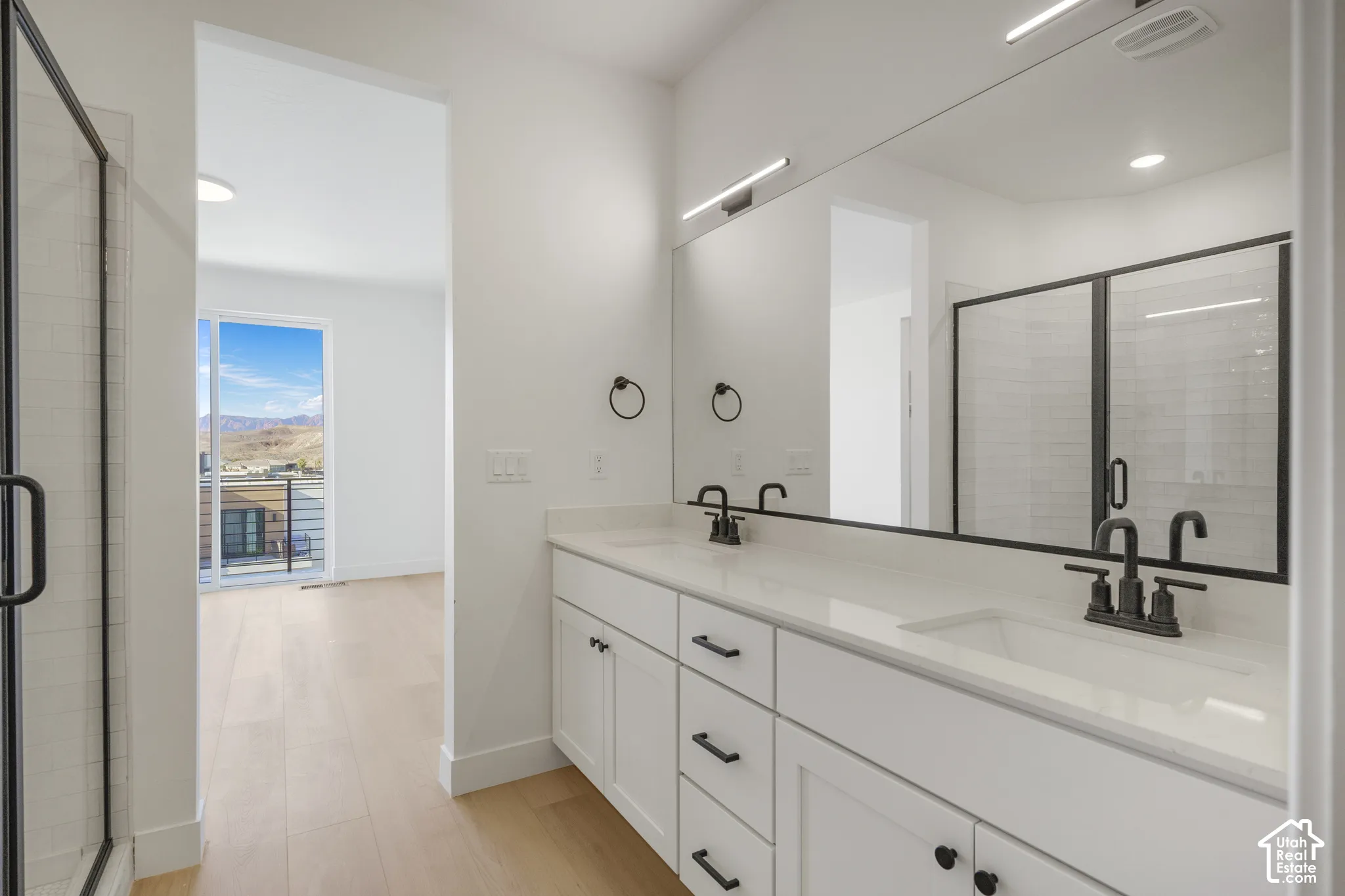 Dual-sink vanity with white cabinetry, light-toned stone-surface countertop, matte black hardware, and an expansive wall-mounted mirror