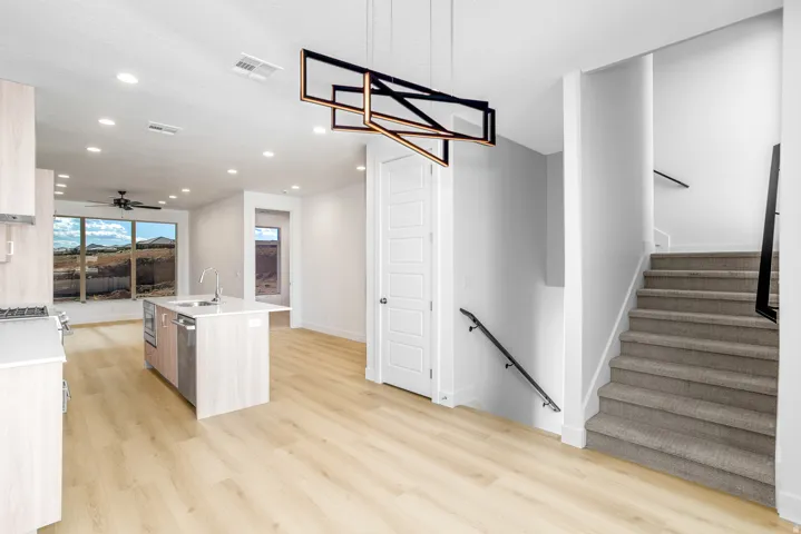 Kitchen with an island with sink, ceiling fan, light wood finished floors, and light stone counters