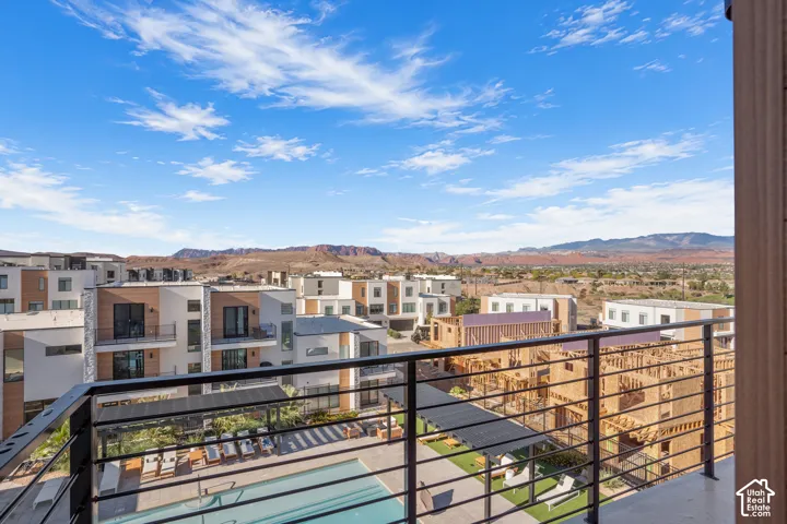 Balcony with a black metal railing overlooking a community swimming pool, pergola-covered hardscaping, and a mountainous landscape backdrop
