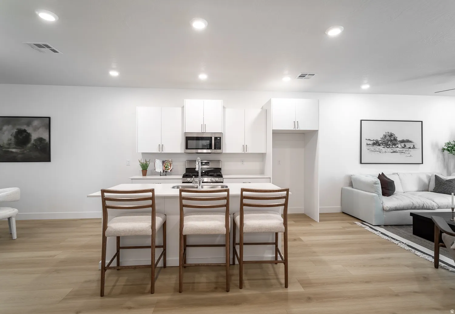 Kitchen with white cabinetry, light wood finished floors, a kitchen bar, an island with sink, and recessed lighting