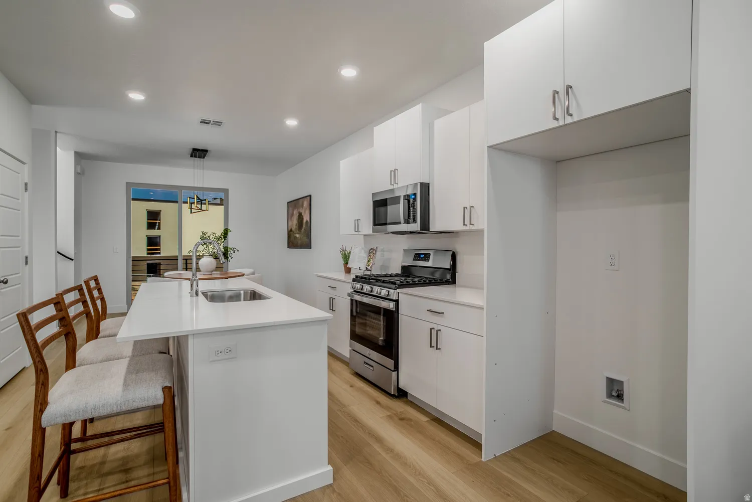 Kitchen with a center island with sink, a breakfast bar, stainless steel appliances, white cabinets, and light wood-type flooring