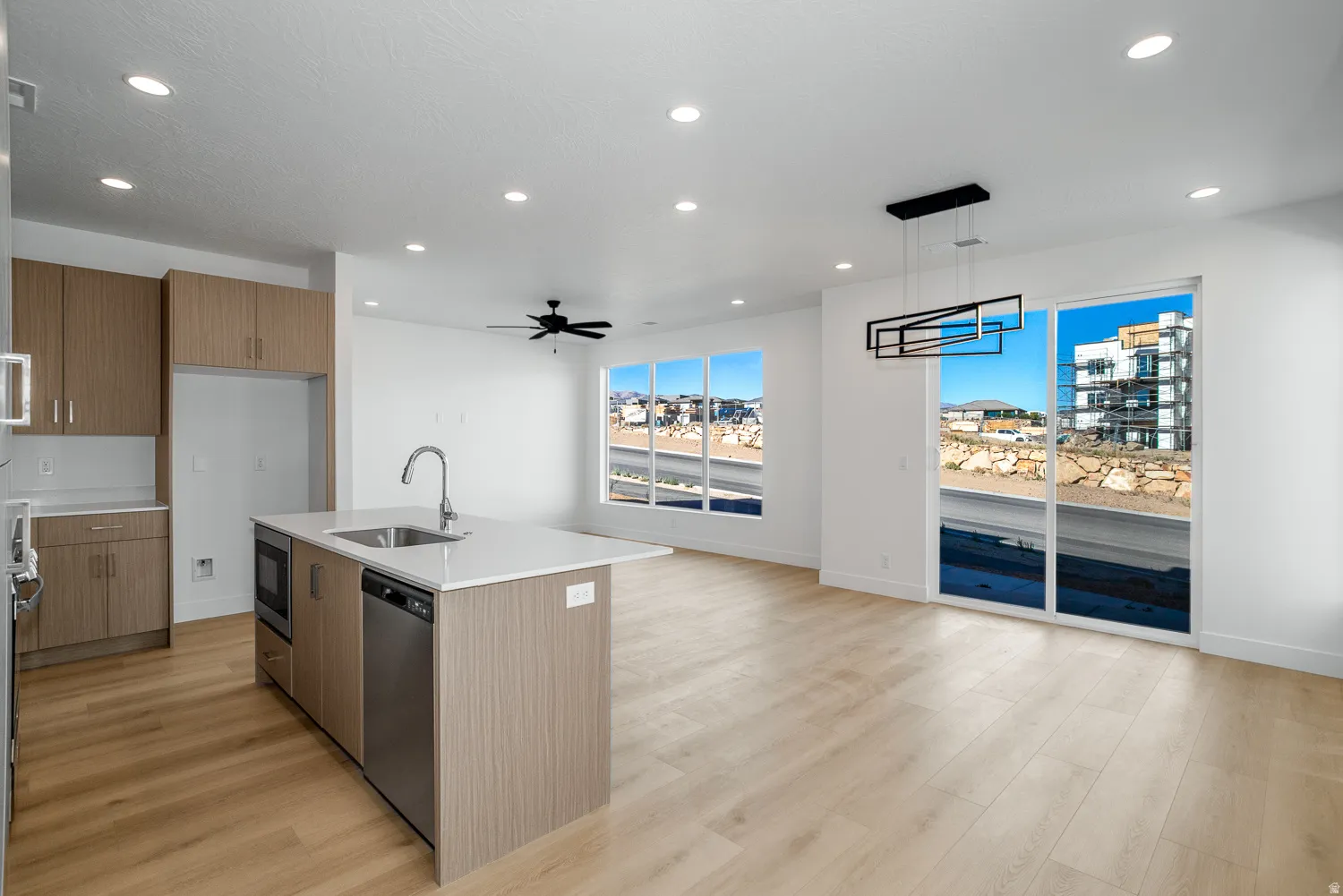 Kitchen featuring modern cabinets, a center island with sink, light stone counters, wood finish cabinets, and pendant lighting