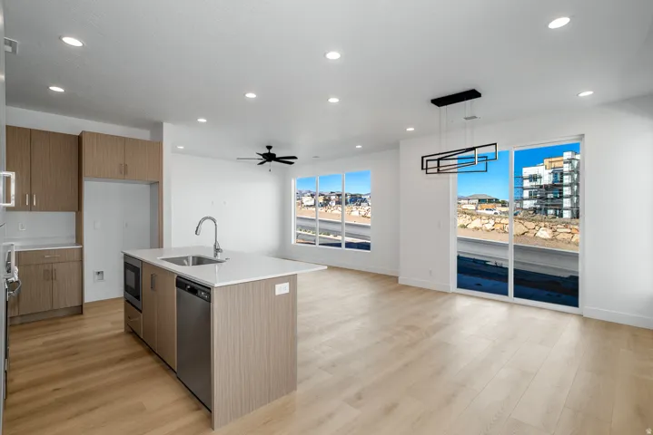 Kitchen featuring modern cabinets, a center island with sink, light stone counters, wood finish cabinets, and pendant lighting