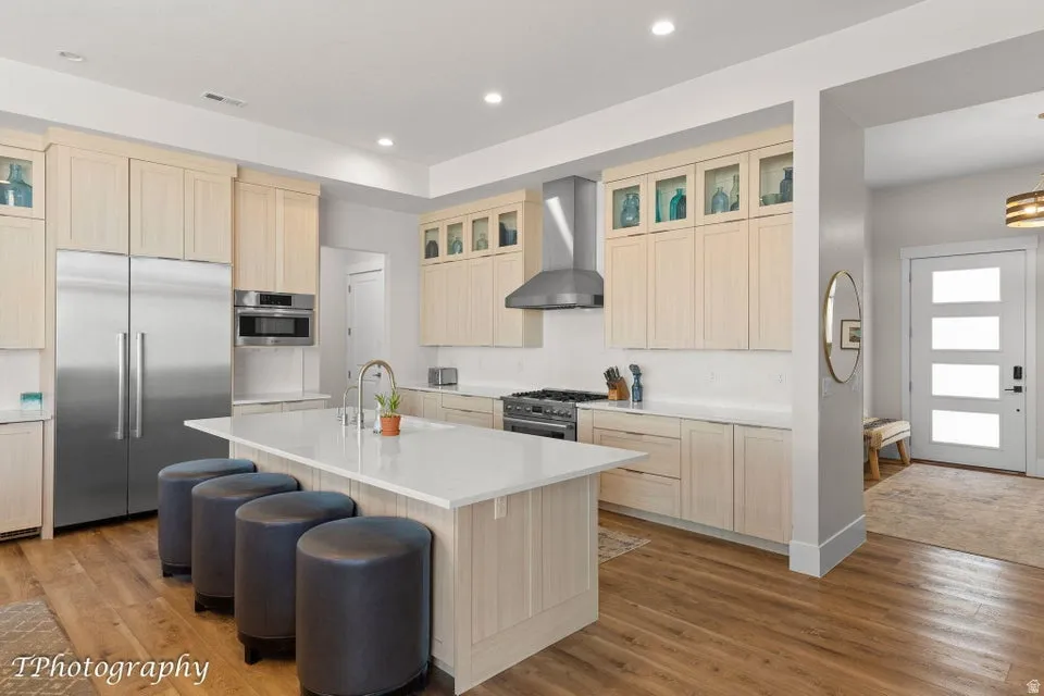 Kitchen with glass fronted cabinets, light wood finish cabinets, high end appliances, a center island with sink, and light wood finished floors