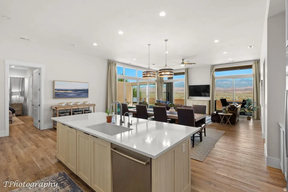Kitchen with light wood-type flooring, open floor plan, dishwasher, a center island with sink, and light stone counters