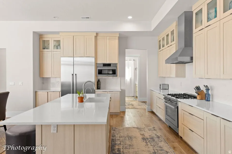 Kitchen with light wood finish cabinetry, glass fronted cabinets, premium appliances, an island with sink, and light wood-type flooring