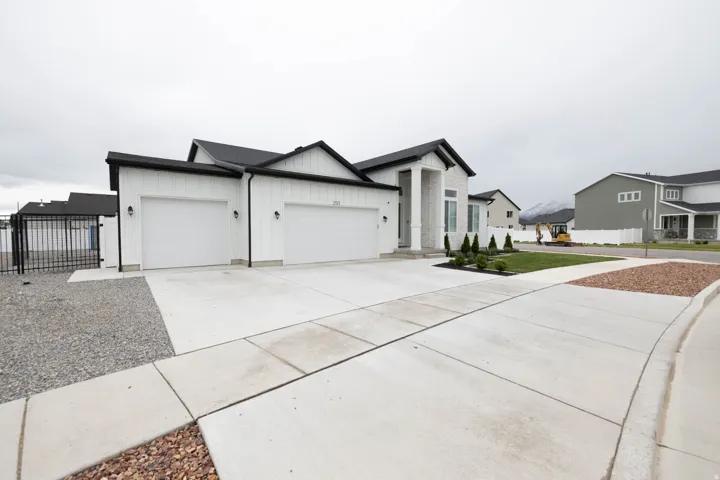 View of front of property with board and batten siding, an attached garage, driveway, and a gate