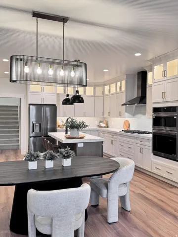 Kitchen featuring hanging light fixtures, light wood-style flooring, an island with sink, a breakfast bar area, and glass fronted cabinets