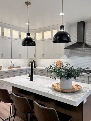 Two tone kitchen featuring a breakfast bar area, glass insert cabinets, backsplash, decorative light fixtures, and two tone color scheme