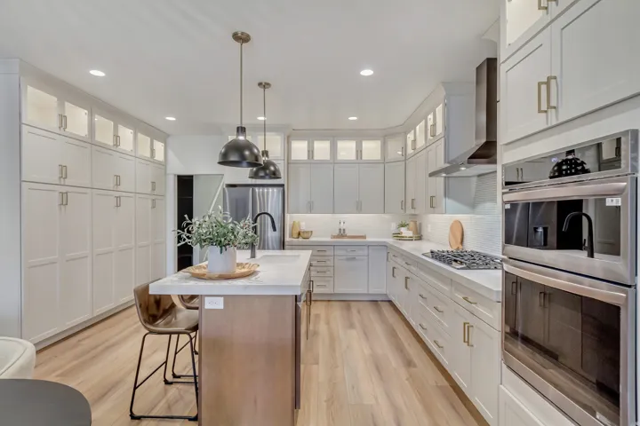 Two tone kitchen featuring stainless steel appliances, glass insert cabinets, a center island with sink, pendant lighting, and two tone color scheme