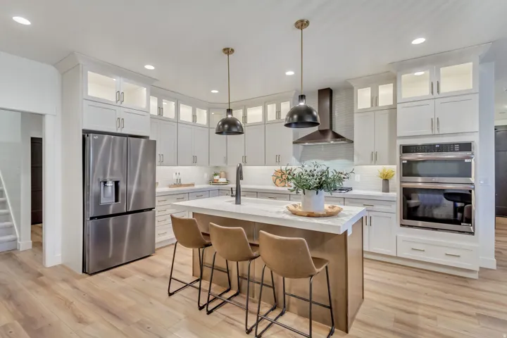 Kitchen featuring stainless steel appliances, hanging light fixtures, a center island with sink, a breakfast bar area, and white cabinetry