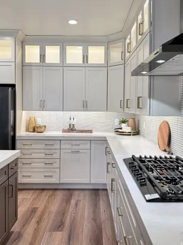 Kitchen with black appliances, light wood-style floors, decorative backsplash, glass insert cabinets, and two tone color scheme