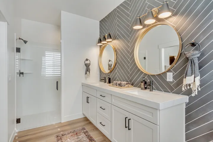 Full bathroom with double vanity, a stall shower, light wood-style floors, and an accent wall