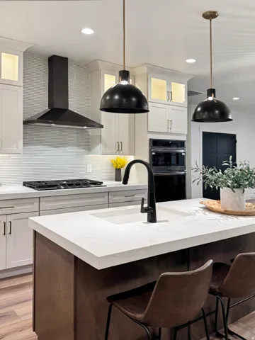 Two tone kitchen with glass insert cabinets, decorative light fixtures, decorative backsplash, light stone countertops, and dual tone cabinetry