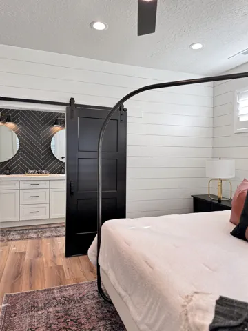Bedroom with a textured ceiling, a barn door, light wood-type flooring, recessed lighting, and wooden walls