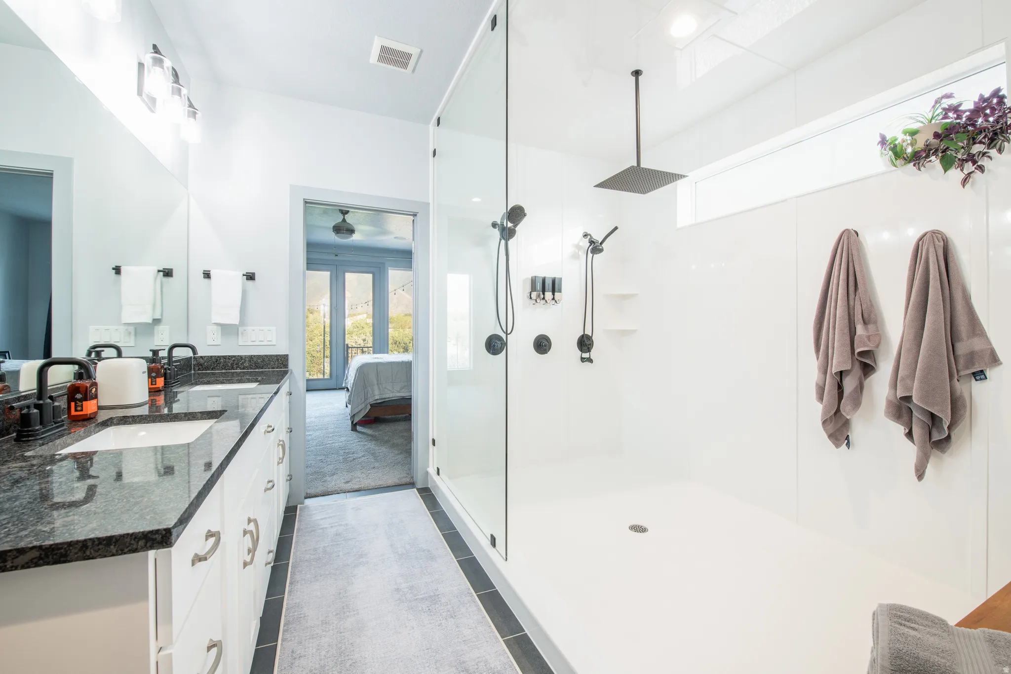 Dual vanity with dark stone-finish countertops, white cabinetry, and matte black fixtures
