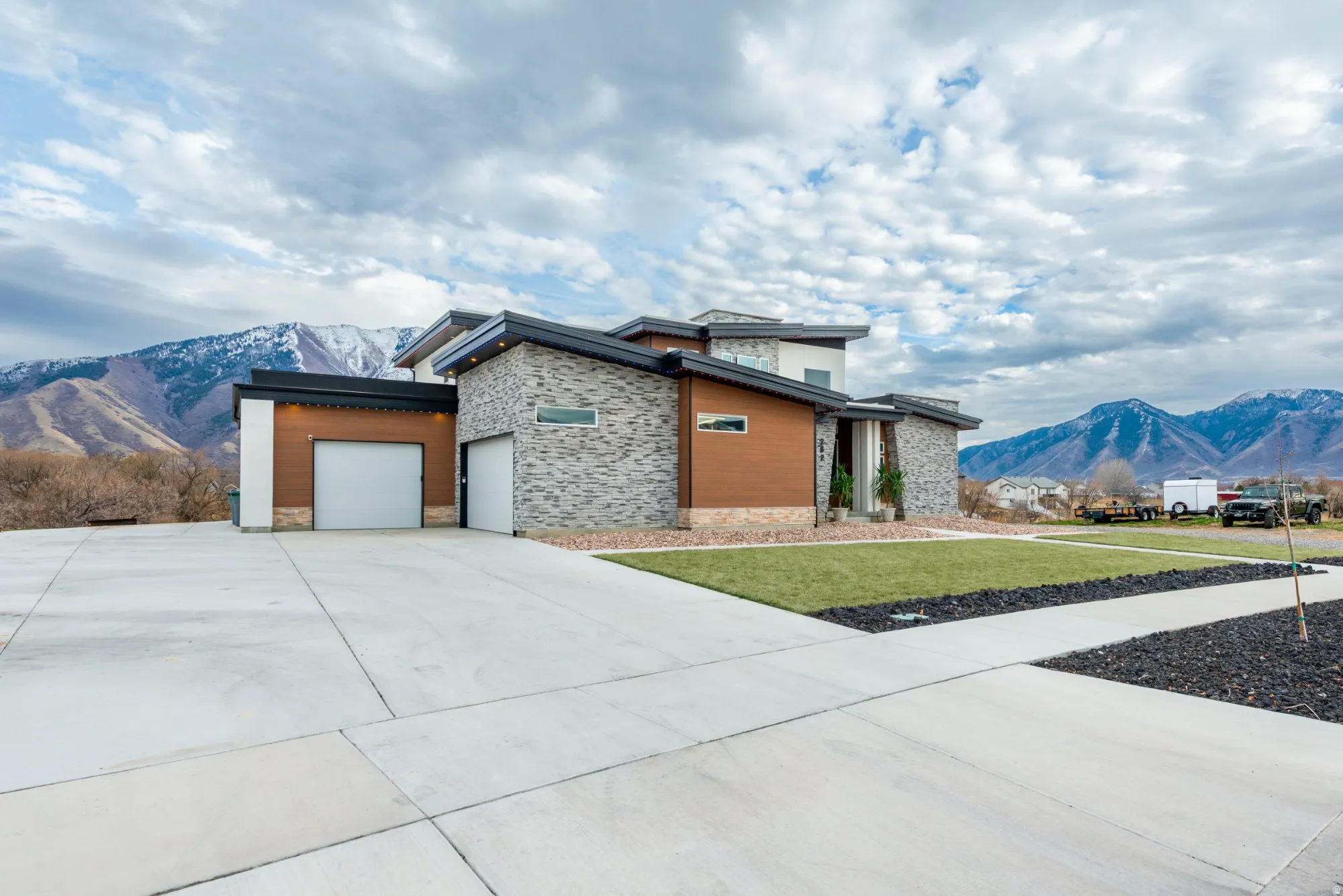 Modern home featuring a mountain view, stone siding, a garage, a front yard, and driveway