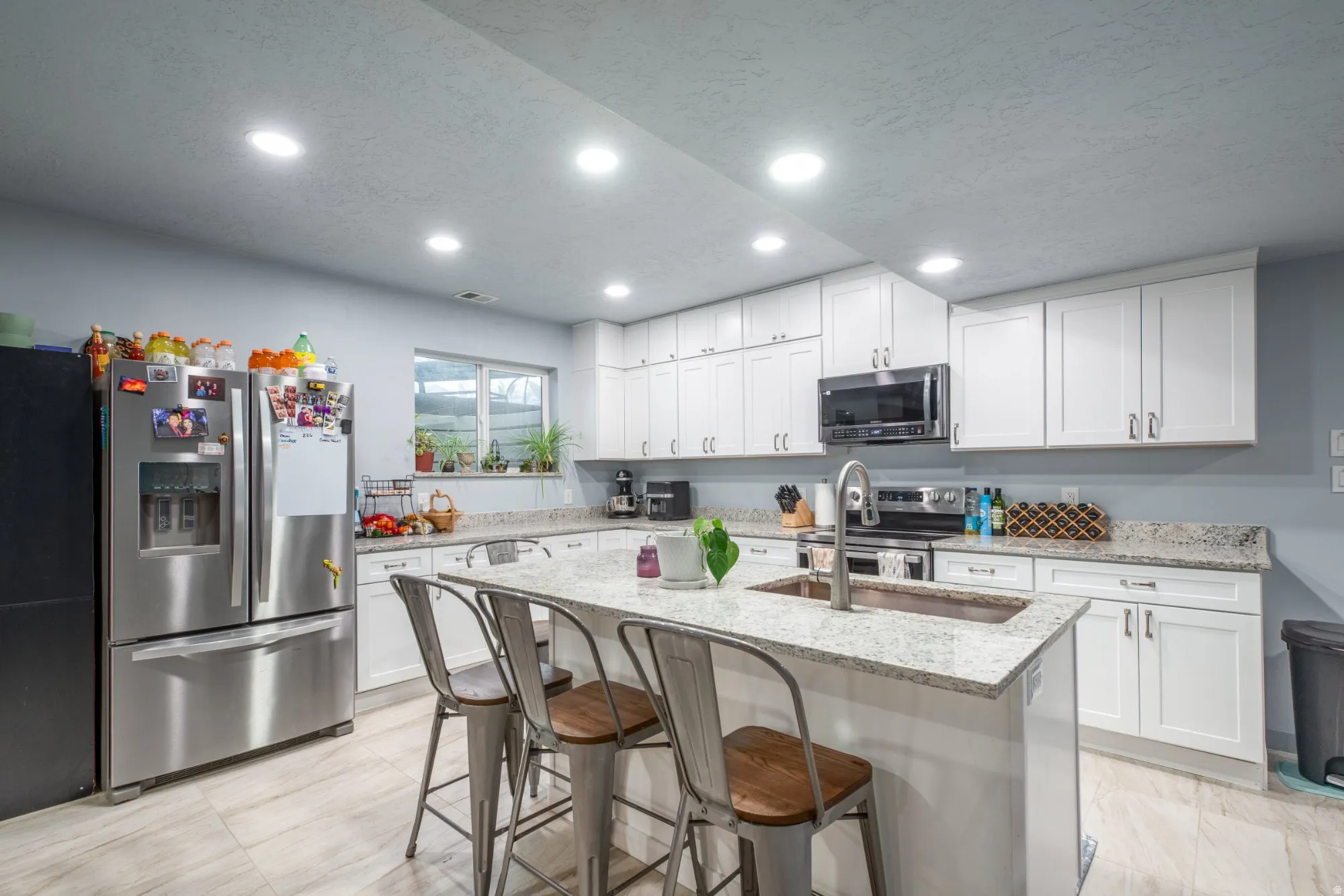 Kitchen with light stone countertops, stainless steel appliances, white cabinets, a breakfast bar area, and a center island with sink