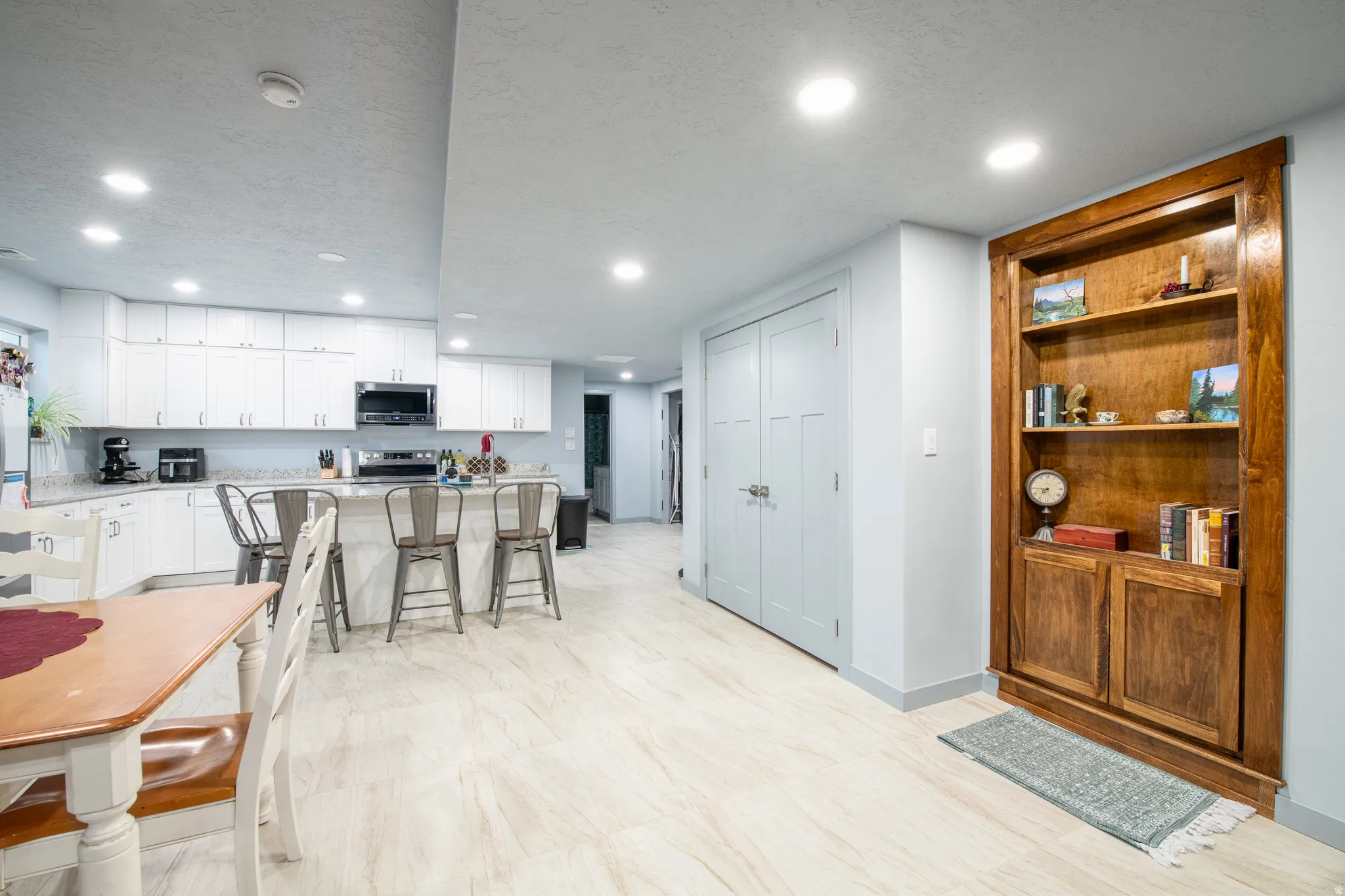 Recessed lighting illuminates the space, featuring a kitchen with white cabinetry, a center island, and integrated appliances