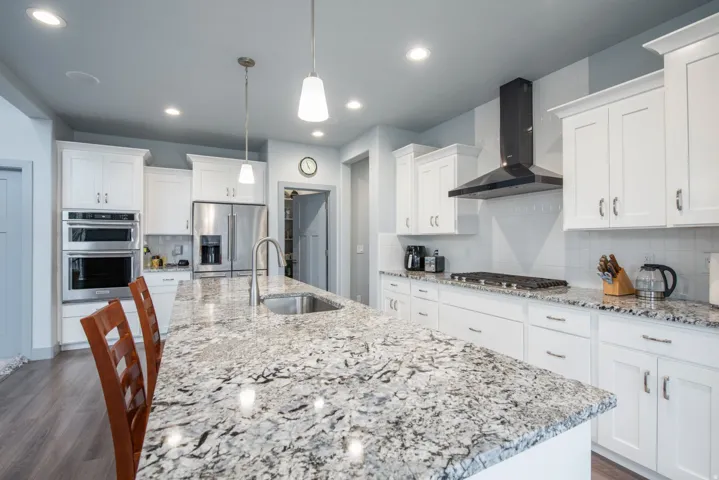 Kitchen featuring a breakfast bar, white cabinets, light stone counters, stainless steel appliances, and decorative backsplash