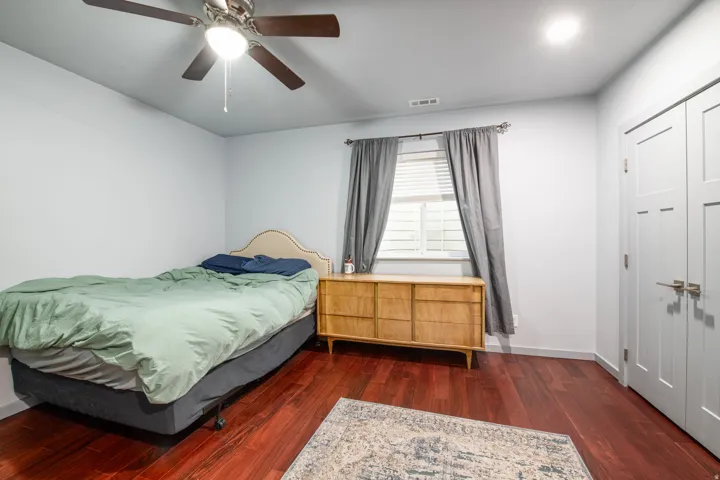 Rich wood-finish flooring, recessed ceiling light, ceiling fan with integrated lighting, and a window with blinds