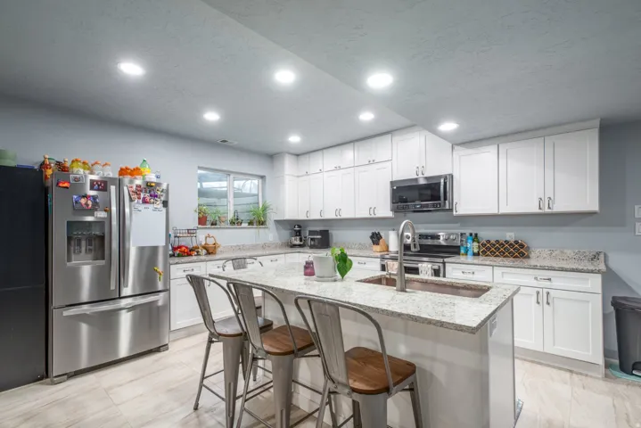 Kitchen with light stone countertops, stainless steel appliances, white cabinets, a breakfast bar area, and a center island with sink