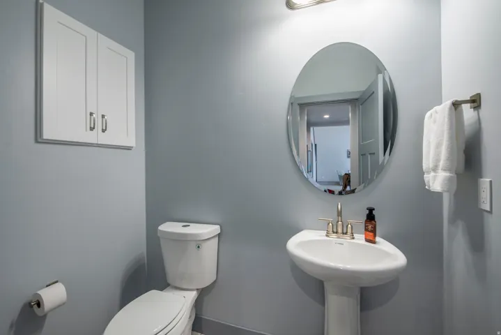 Pedestal sink with a brushed nickel faucet, oval mirror, wall-mounted cabinetry, and a toilet