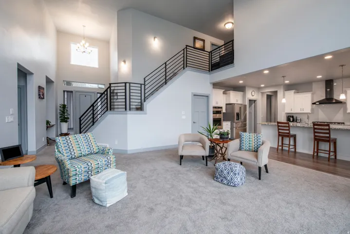 Two-story ceiling, contemporary staircase with horizontal black metal railings, white kitchen cabinetry, stainless steel appliances, and a granite-style countertop on a central island
