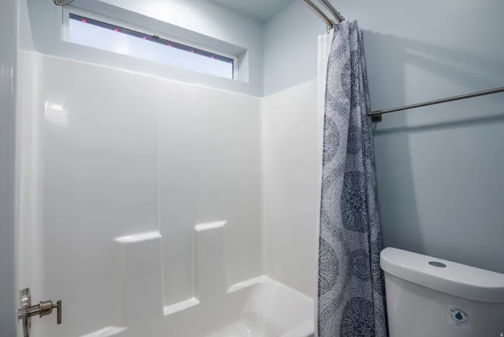 Bathtub with white surround, chrome shower fixtures, and overhead transom window