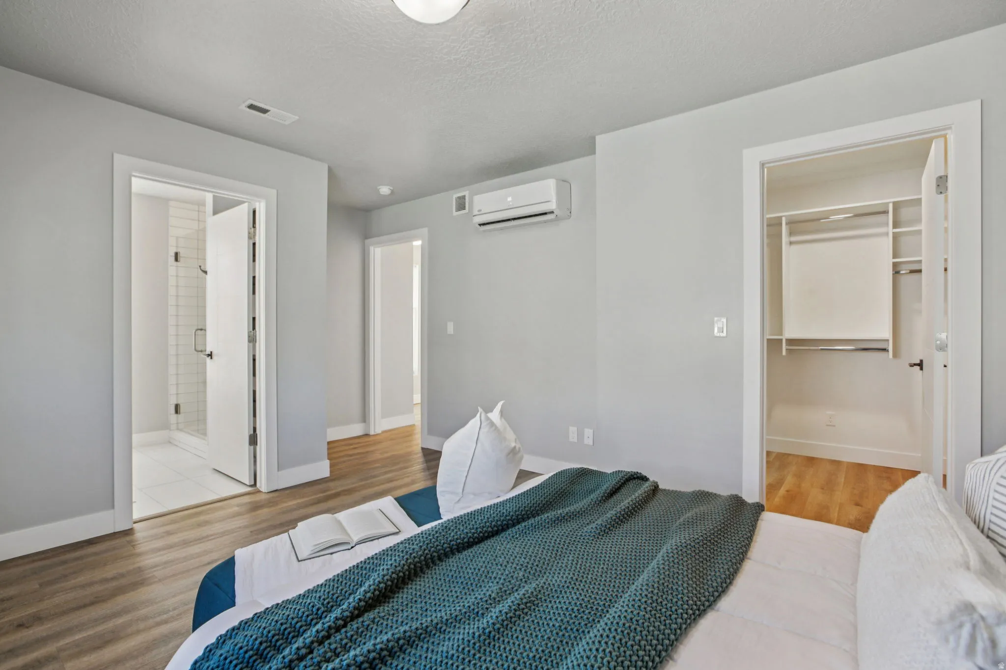 Bedroom with a spacious closet, light wood finished floors, ensuite bath, and a textured ceiling
