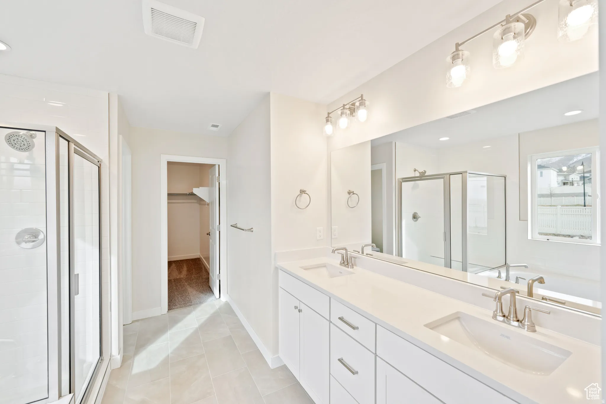 Bathroom featuring a walk in closet, double vanity, a stall shower, recessed lighting, and light tile patterned flooring