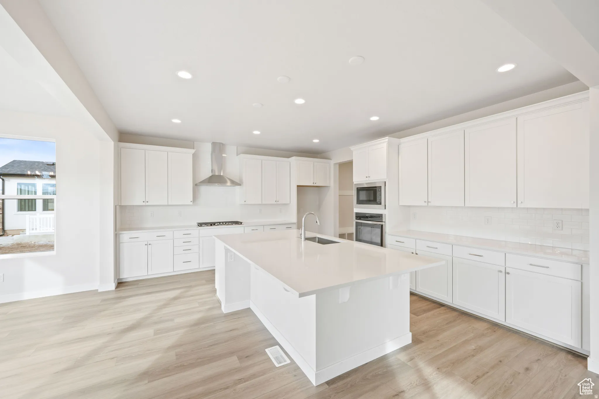 Kitchen with white cabinets, an island with sink, light wood-style flooring, stainless steel appliances, and recessed lighting