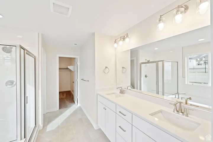 Bathroom featuring a walk in closet, double vanity, a stall shower, recessed lighting, and light tile patterned flooring