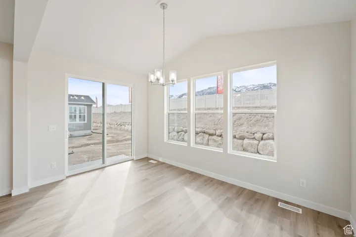 Unfurnished dining area featuring a chandelier, vaulted ceiling, and light wood finished floors