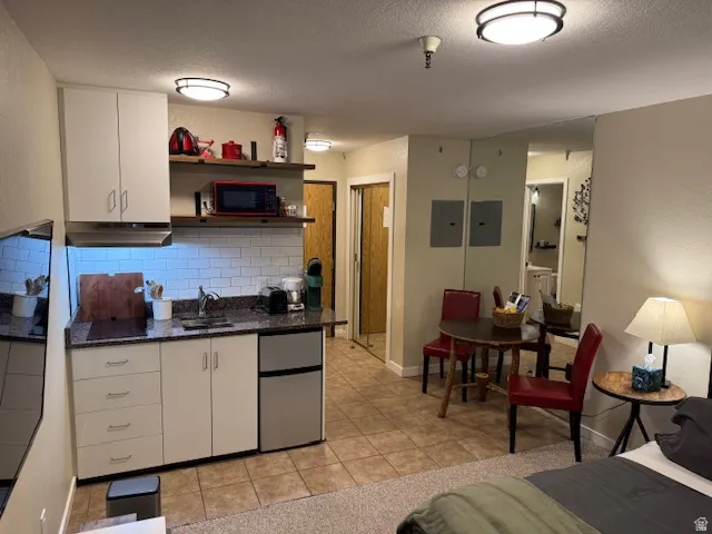 Kitchen with stainless steel fridge, dark stone countertops, light tile-patterned floors, an electric induction panel, and a dining area