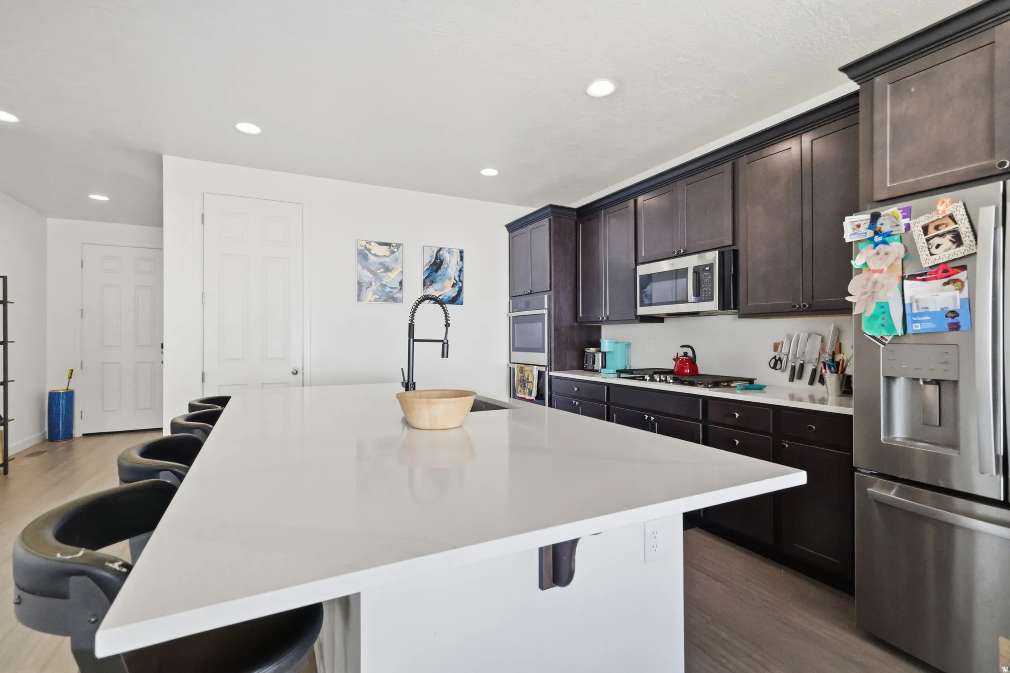 Kitchen featuring a kitchen breakfast bar, stainless steel appliances, dark wood finish cabinets, wood floors, and recessed lighting