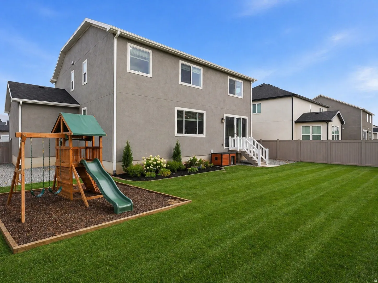 Back of property with a fenced backyard, a playground, and stucco siding