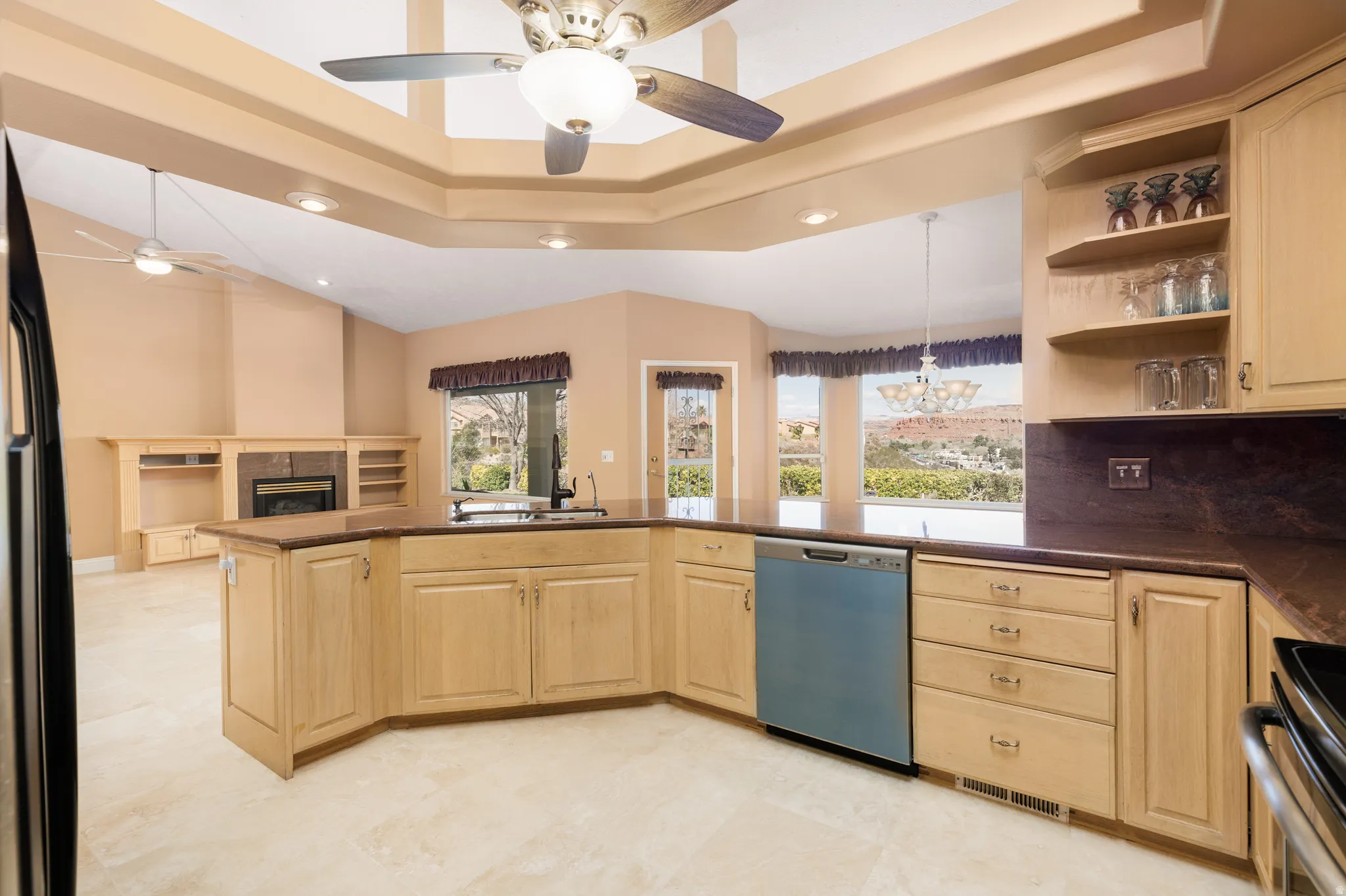 Kitchen with light wood finish cabinetry, a raised ceiling, dishwashing machine, stainless steel range, and a ceiling fan