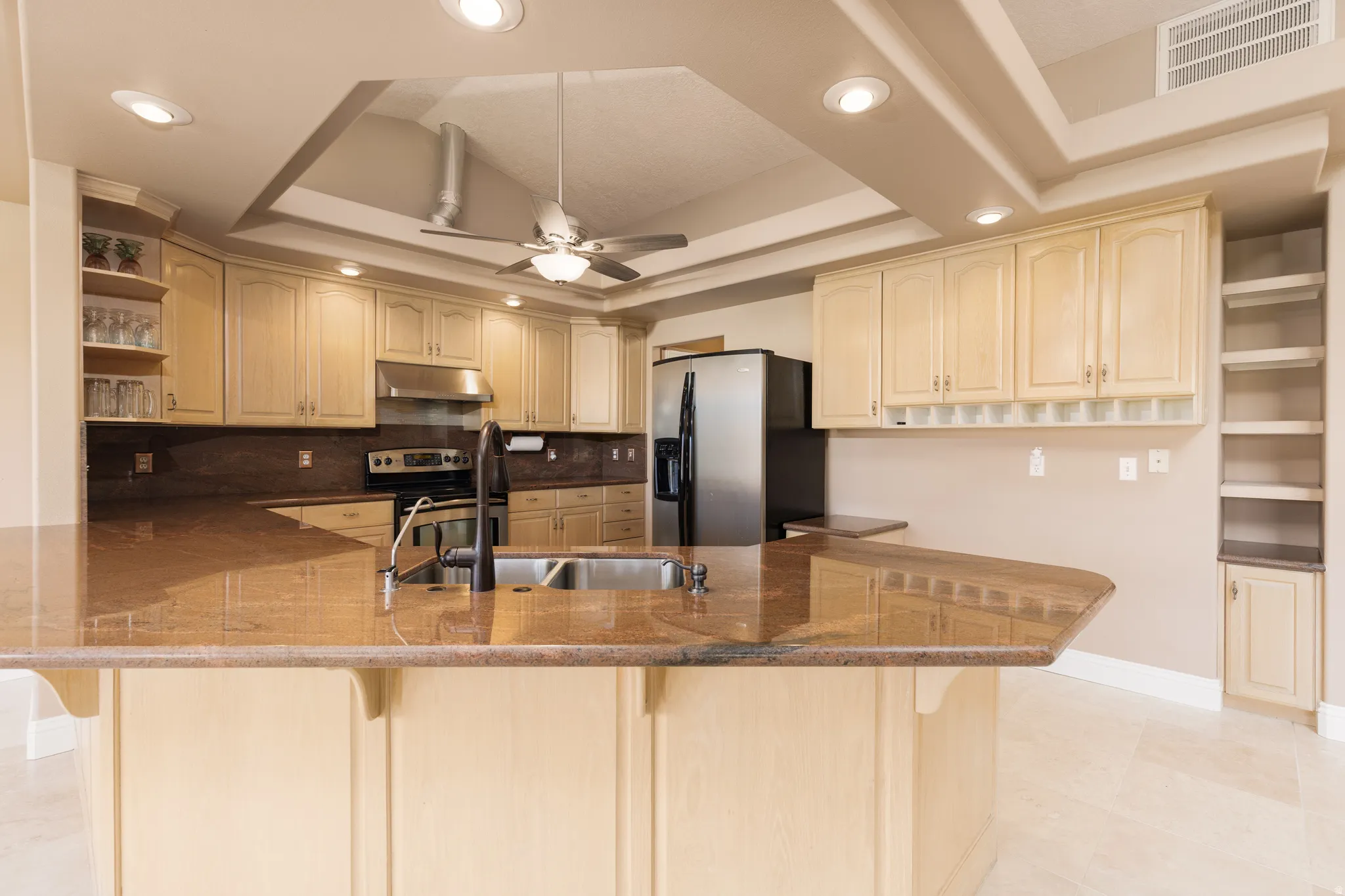 Kitchen with open shelves, a breakfast bar, recessed lighting, stainless steel appliances, and a raised ceiling