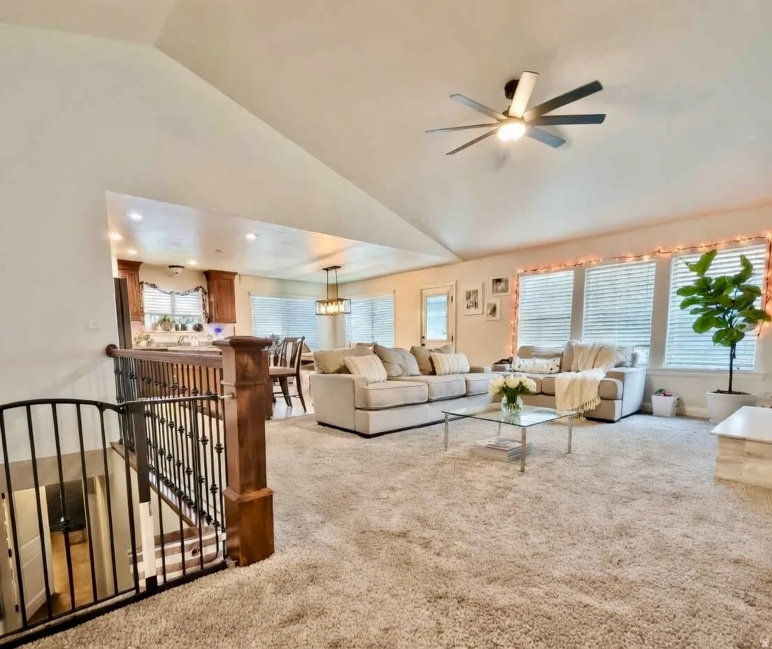Carpeted living area with a ceiling fan, vaulted ceiling, and suspended lighting