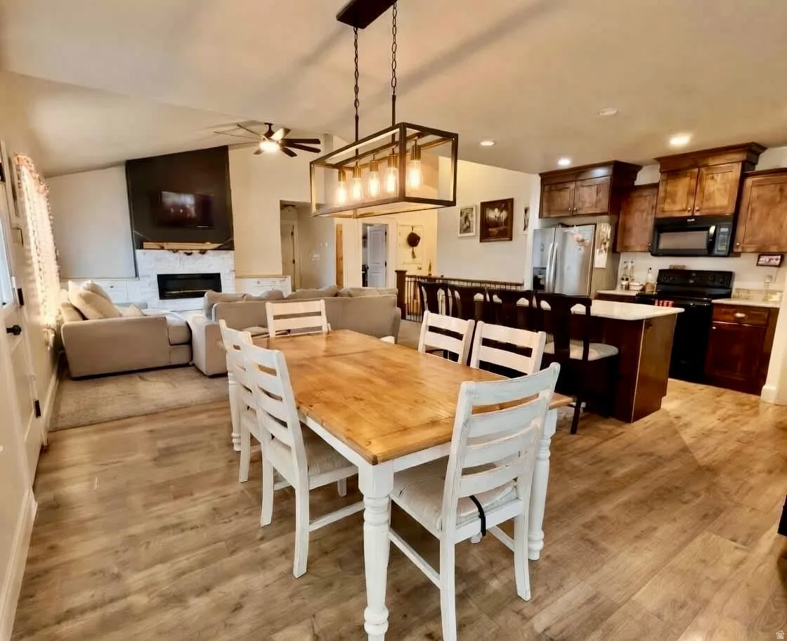 Dining space featuring a ceiling fan, light wood-style flooring, a stone fireplace, vaulted ceiling, and recessed lighting