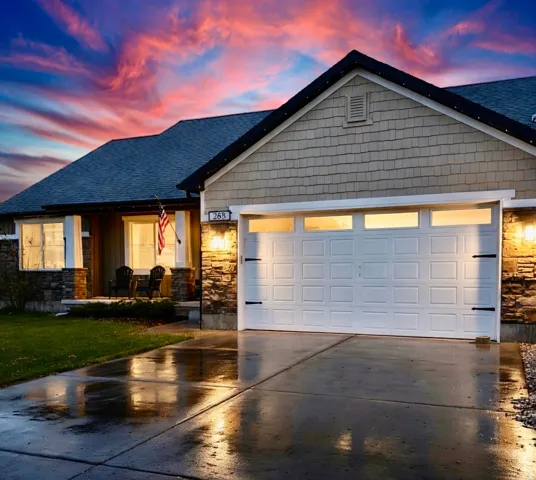 View of front facade with stone siding, driveway, an attached garage, and covered porch