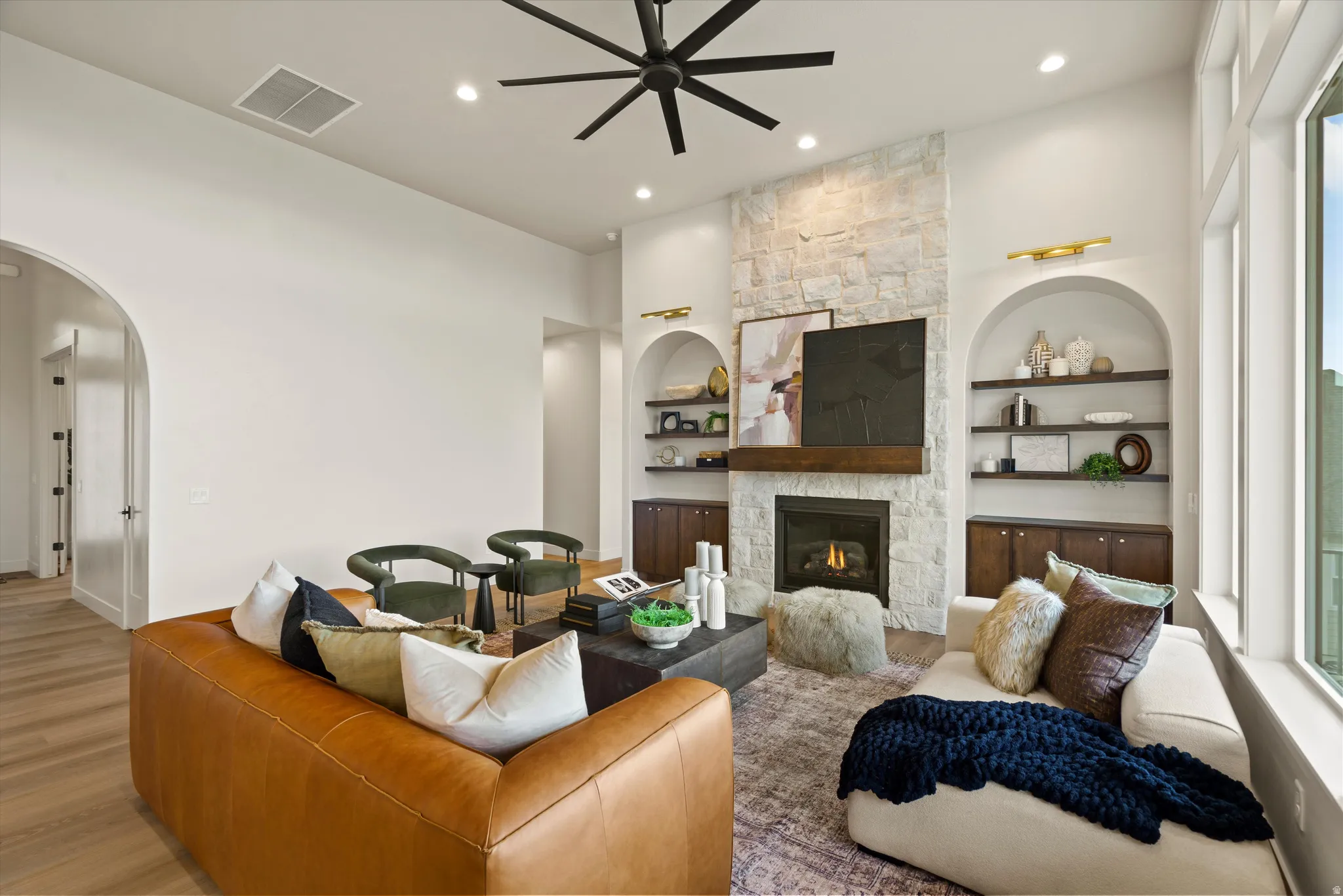 Living room with arched walkways, wood finished floors, built in features, ceiling fan, and a fireplace